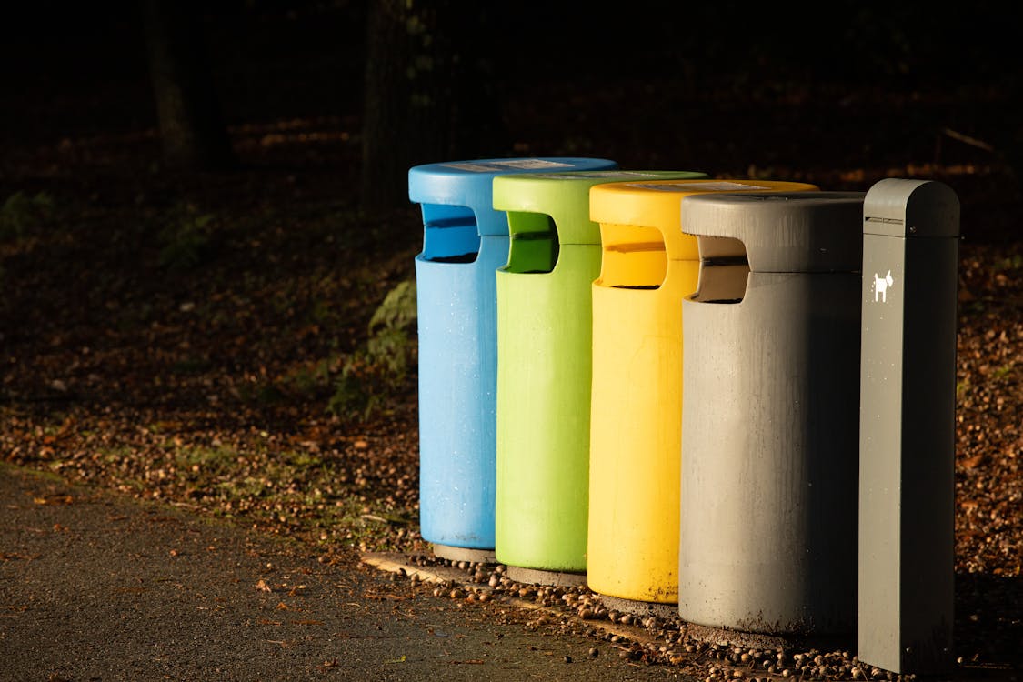 Blue green yellow and gray recycling bins lined up for waste sorting on a pathway, representing apartment community recycling programs