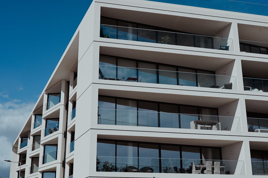 Modern white apartment building exterior with glass balconies against a blue sky, representing the type of multifamily community that offers premium amenities like valet trash